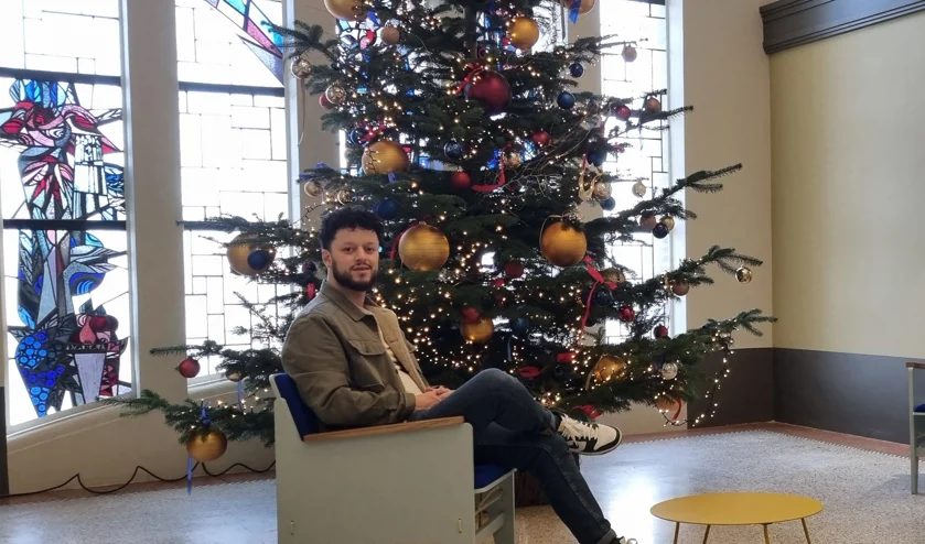 Foto van Bilal El Amraoui zittend in een stoel voor een kerstboom in het Innovatie Kwartier Den Bosch