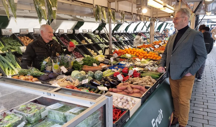 Foto van Marcel Ploegmakers in gesprek met een markt koopman op de Markt