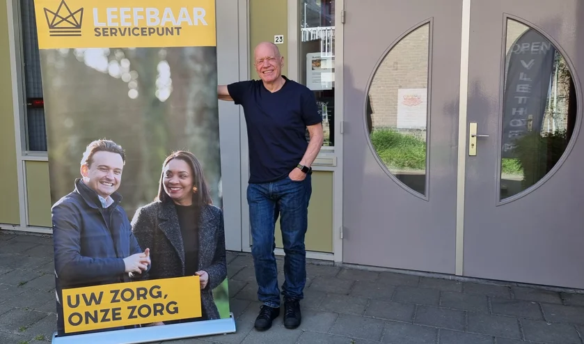 Foto van Rinie Mees die bij de Vlethof staat tegen een poster van Leefbaar Servicepunt